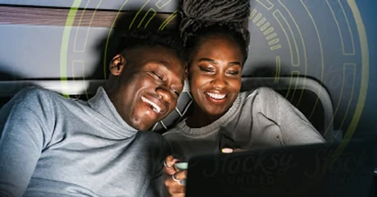 Couple sitting on couch smiling while using tablet